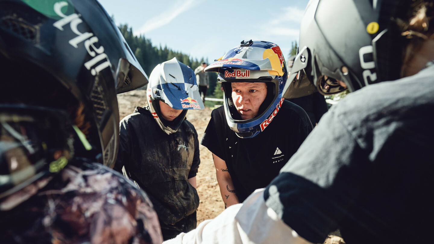 Eine Gruppe von Mountainbikerinnen, alle mit Helmen, steht zusammen und bespricht sich. Sie tragen verschiedene Helme, und sind in sportlicher Ausrüstung.