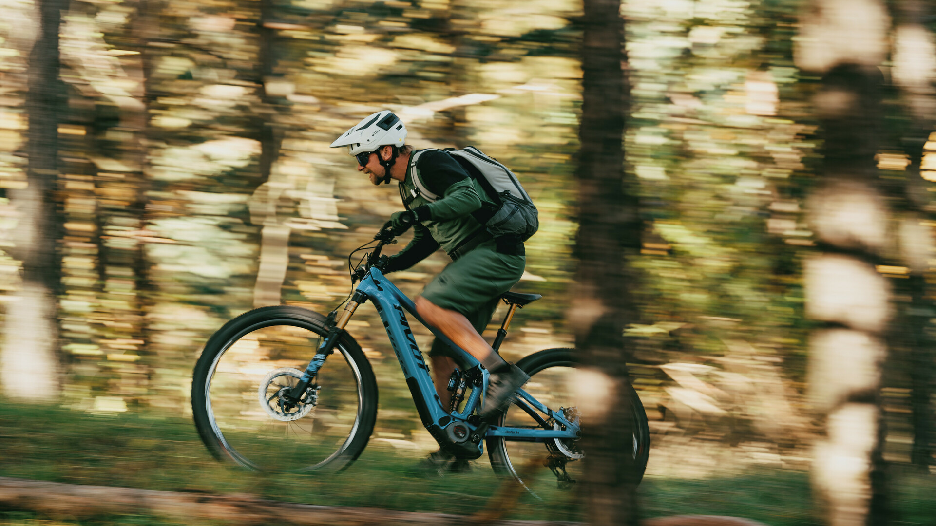 Vététiste portant un casque et un sac à dos roule à grande vitesse à travers une forêt sur un vélo bleu.